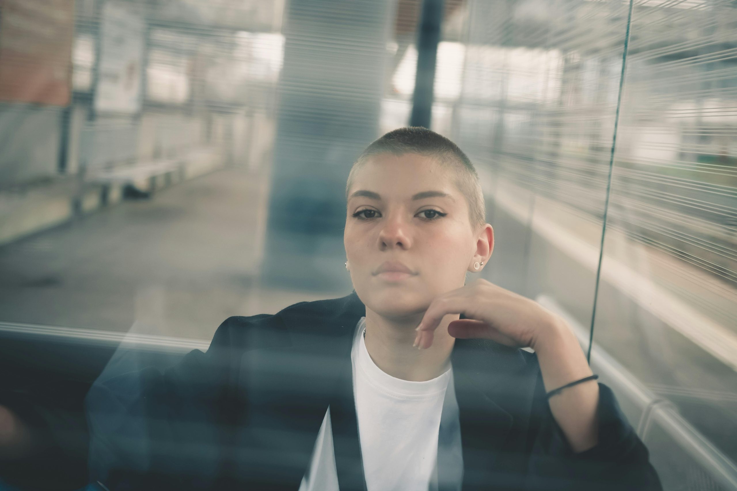 Thoughtful woman with short hair sits introspective behind glass panel.